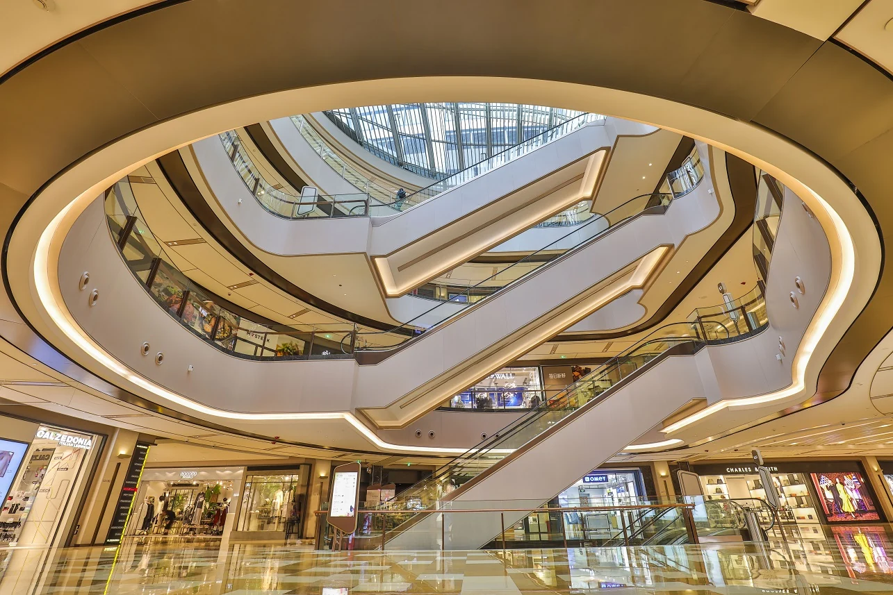 Curved pale balconies and escalators beneath the skylight inside Shanghai’s HKRI Taikoo Hui shopping mall.