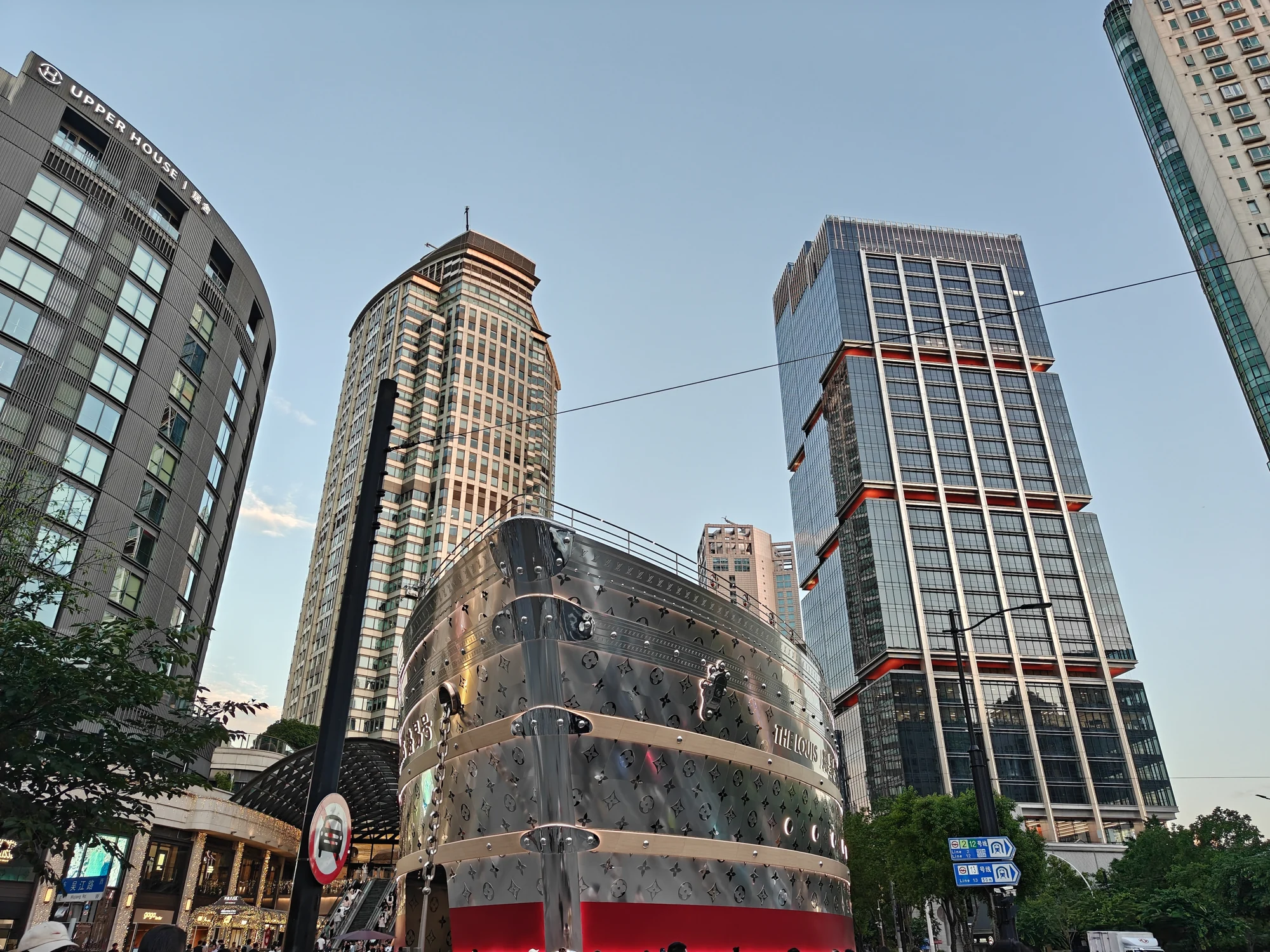 The Louis in Shanghai at dusk, with visitors and neighbouring towers visible around its metallic ship-shaped facade.