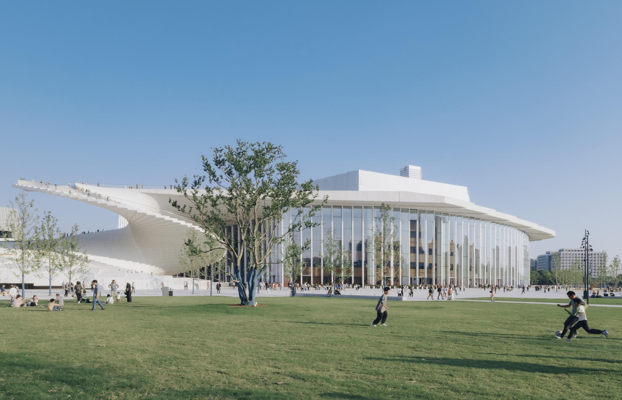 Visitors on the lawn beside the Shanghai Grand Opera House’s glass lobby and white spiral staircase