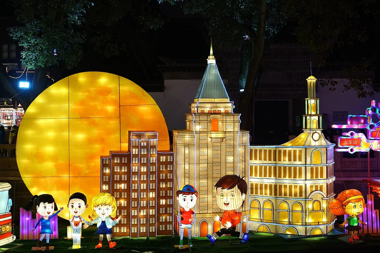 Colourful architectural and character lanterns beside a large glowing yellow disc at Yuyuan.