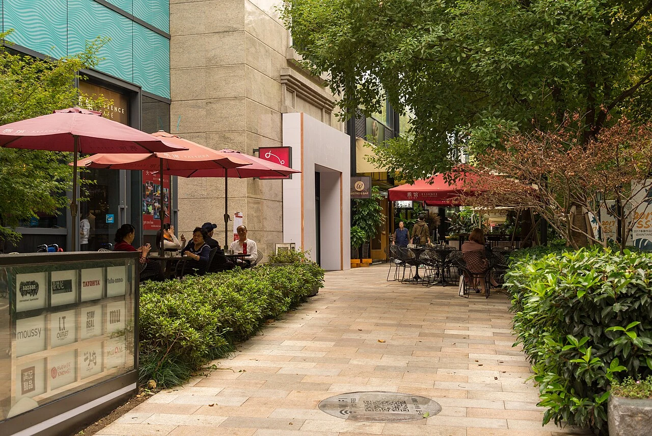 Outdoor tables, red umbrellas and planting in a paved lane at Xintiandi.