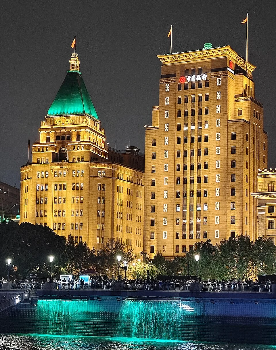 Peace Hotel and neighbouring Bank of China Building seen from the Huangpu at night in April 2026.